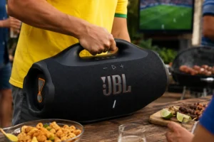 Pessoa segura JBL Boombox 4 do peito para baixo em ambiente de churrasco durante jogo da Copa